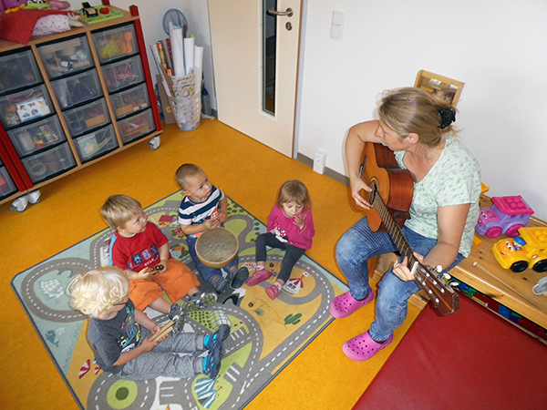 Kinder sitzen mit Erzieherin und singen zur Gitarre