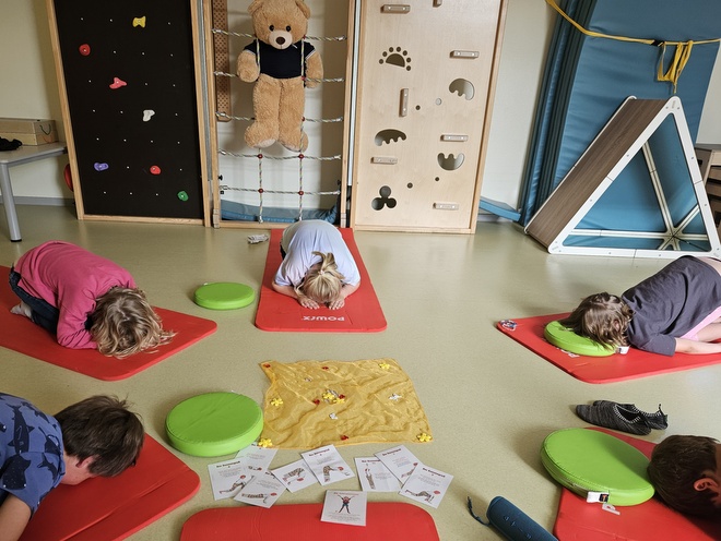 Bild zeigt eine Gruppe von 5 Kindern, welche im Sportraum der Kita auf Yogamatten Entspannungsübungen