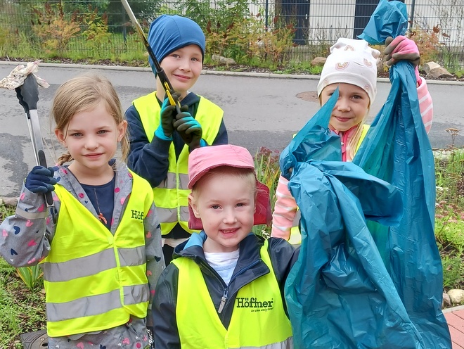 Bild zeigt 4 Kinder mit gelben Warnwesten. Zwei Kinder halten blaue Mülltüten in den Händen und die anderen beiden haben Müllsammelzangen in den Händen.i