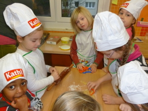 Kinder mit großen Kochmützen stechen Plätzchen aus