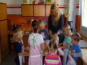 Gruppe von Kindern mit erzieherin beim kochen