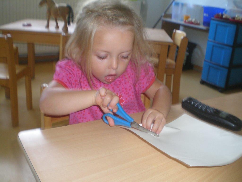 kleines Mädchen schneidet mit einer Schere ein Blatt Papier