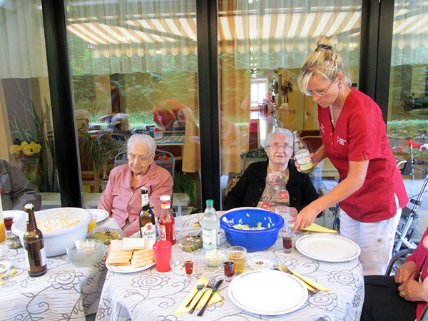 Bewohner und Personal auf der Terrasse am Tisch, eingedeckt mit Essen