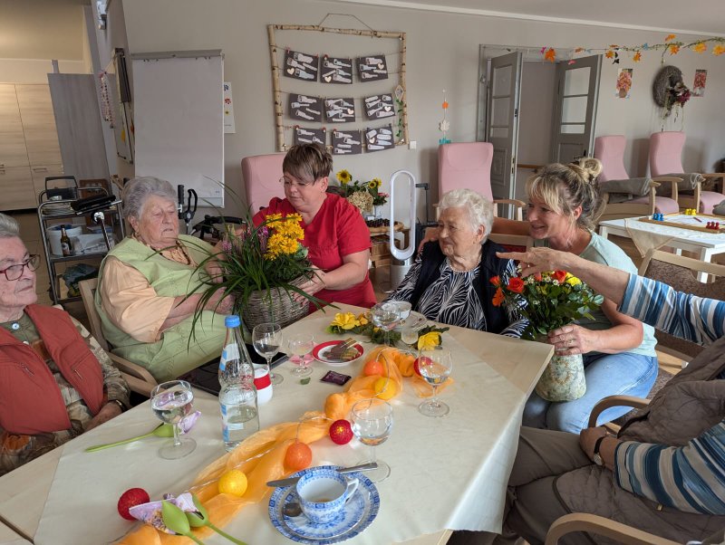 Bild zeigt mehrere Tagesgäste und Mitarbeitende wie sie einer Seniorin zum Geburtstag gratulieren
