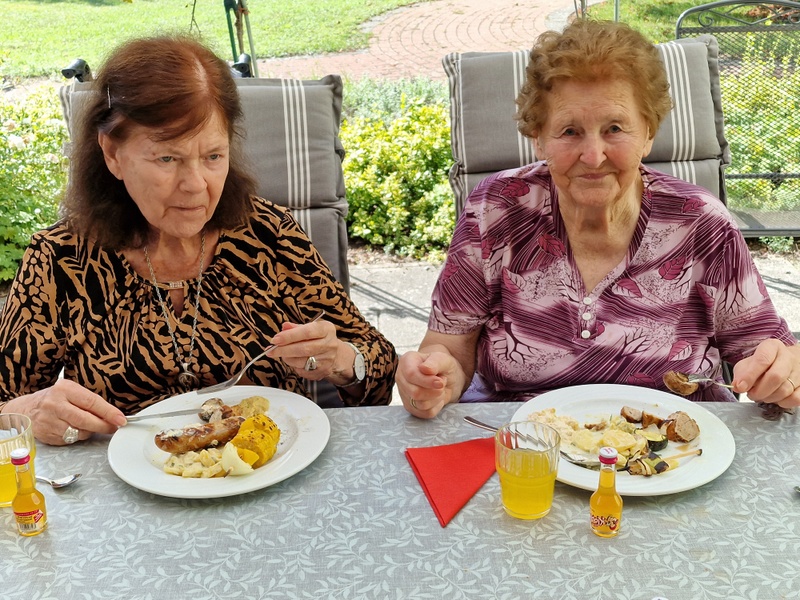 Bild zeigt zwei Seniorinnen am Tisch mit Grillteller und Getränk