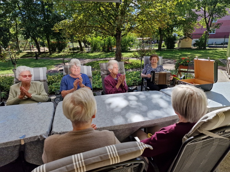 Bild zeigt Senioren am Tisch sitzend und Lieder singen mit Akkordeonbegleitung