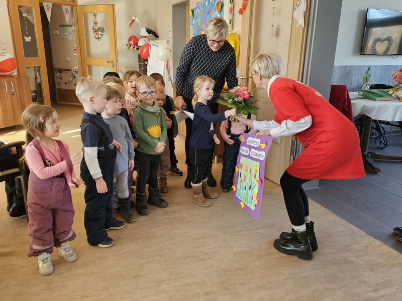 Bild zeigt eine Gruppe Kita-Kinder, welche einen Blumenstrauß und ein selbst gestaltetes Plakat zum 12 jährigen Bestehen übergeben