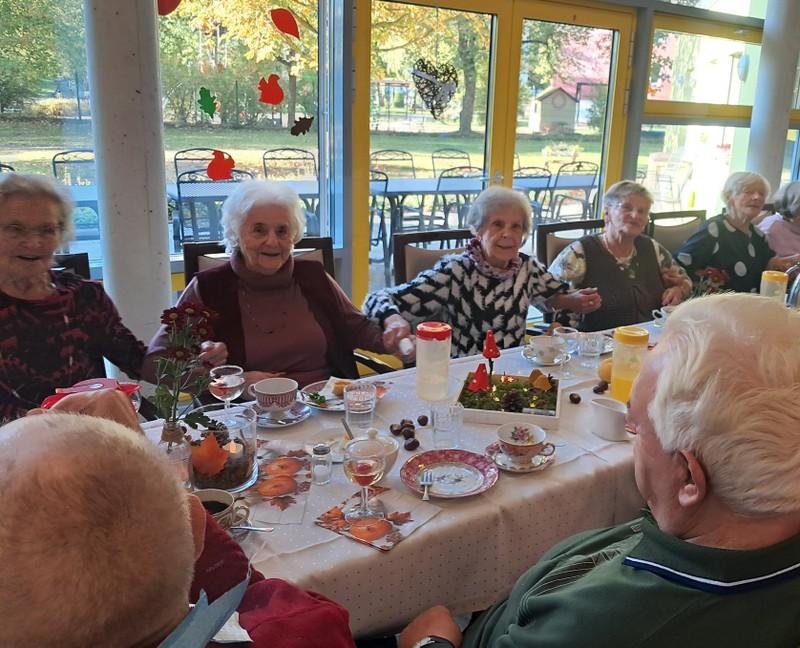 Bild zeigt viele Besucher der Tagespflege an einem schön gedeckten Tisch in einer lustig, fröhlichen Feierrunde.