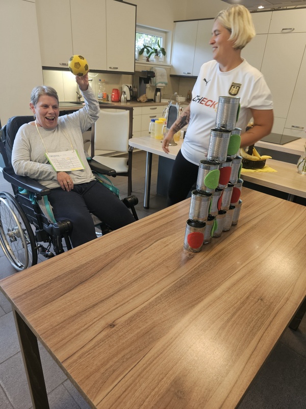 Bild zeigt ein Frau, Tagesgast in der Tagespflege, bei einer sportlichen Aktivität. Sie sitzt im Rollstuhl und macht Dosen werfen