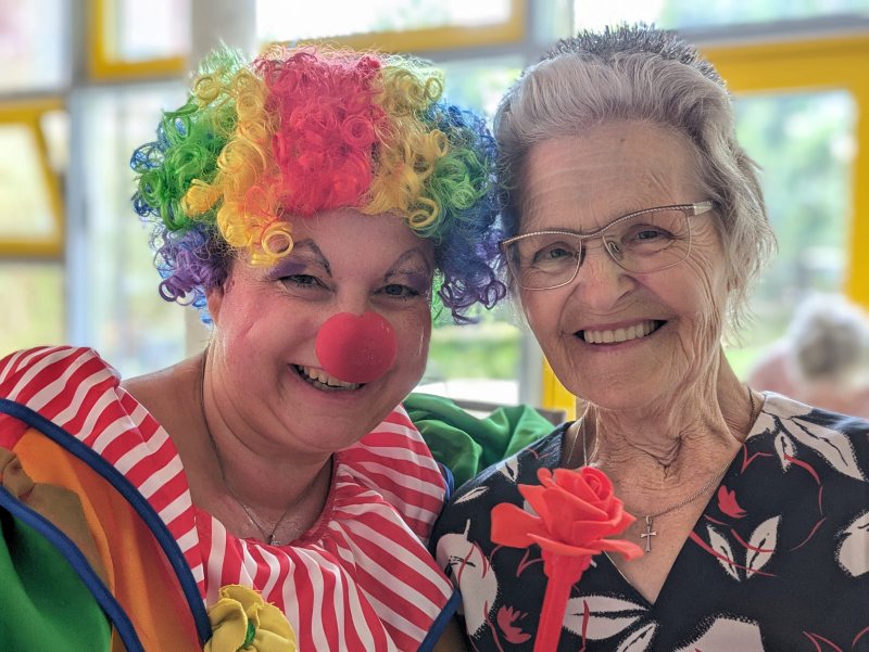 Bild zeigt eine als Clown verkleidete Mitarbeiterin, die mit einem Tagesgast vor der Kamera posiert